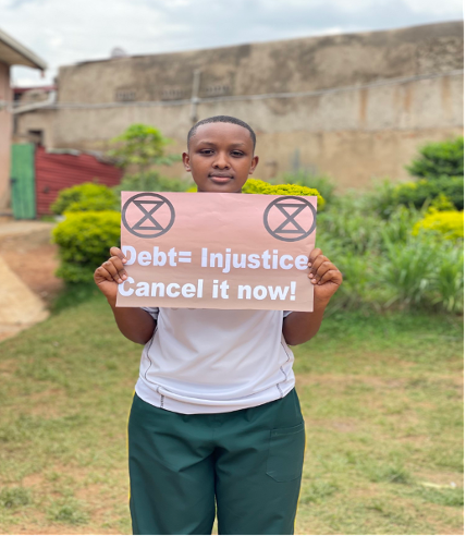 Jovem ativista climática segura um cartaz com os dizeres "Debt = Injustice— Cancel it now!" durante a ação "Cancel the Debt, Heal the Planet" emKigali.